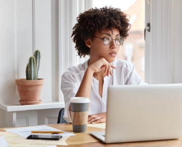 Woman with glasses at laptop with coffee and plant