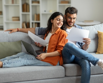 couple sitting on couch looking at papers and laptop