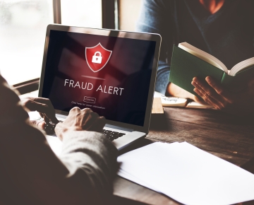 man looking at fraud message on computer and other person at desk looking at book
