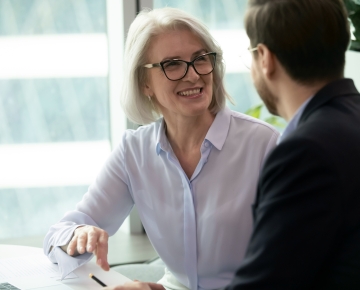 woman in white shirt and glasses discussing something with man in suit