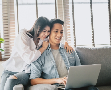 couple looking at laptop on couch with windows in background