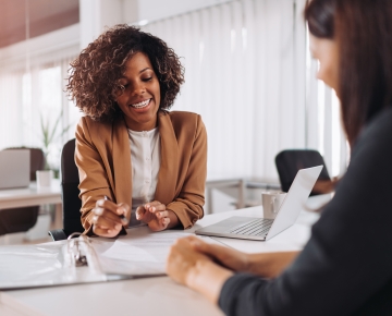 woman explaining documents to other woman in tan sport coat