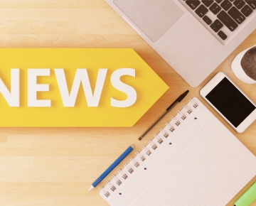 News on desk with laptop, phone, coffee, paper, and pens