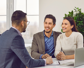 couple meeting with man in office with laptop on desk and plant in background