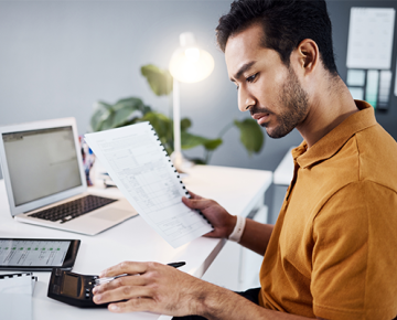 man in yellowish orange shirt reviewing papers at his desk